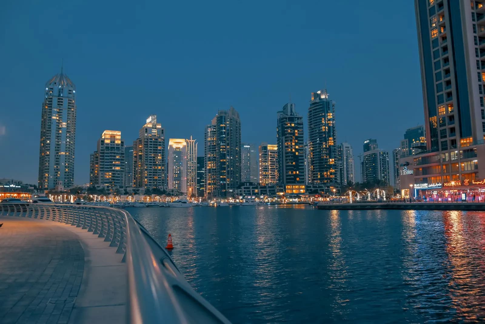 The Dubai Marina promenade at dusk, towers lit along the water.
