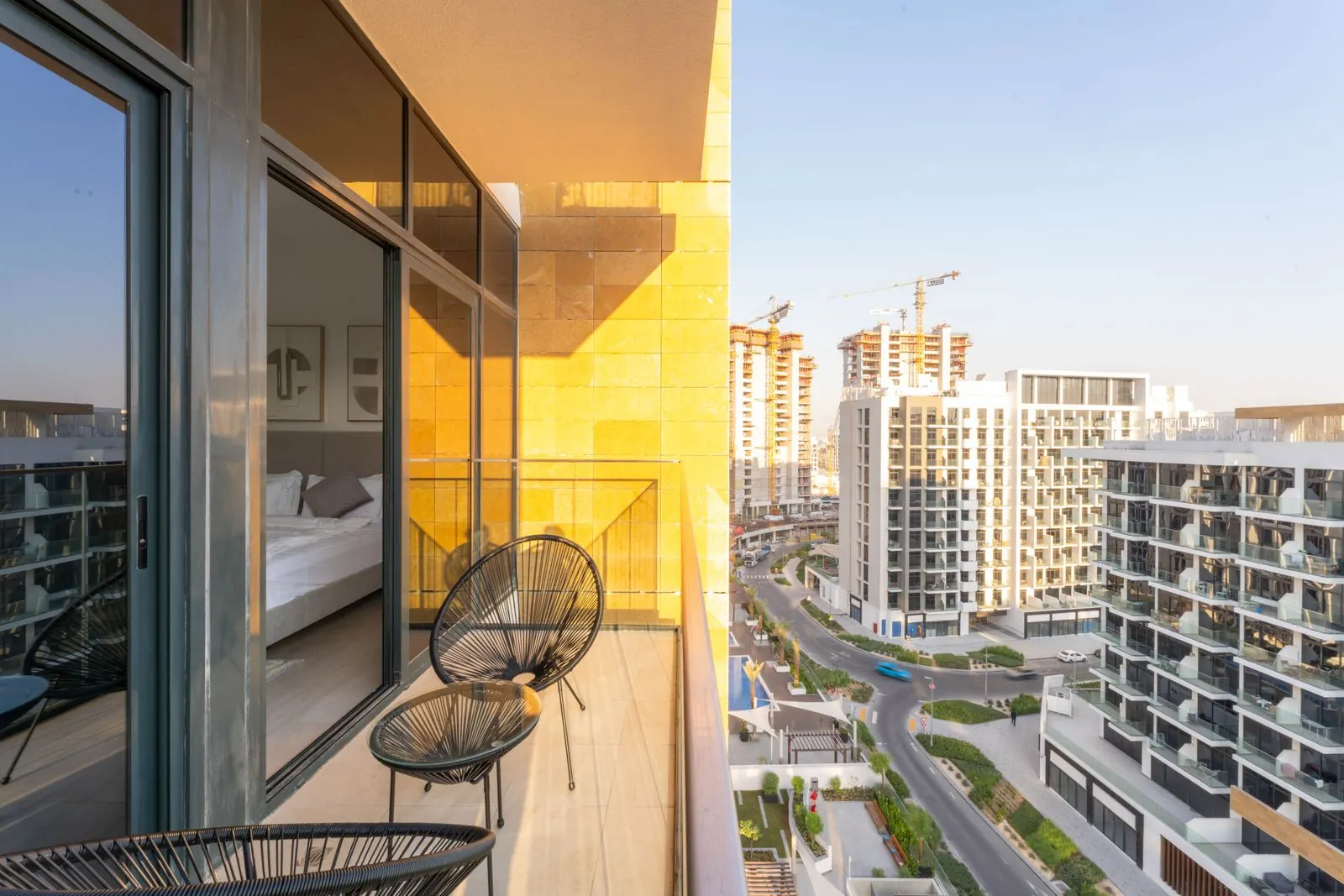 شرفة مرتفعة بكراسٍ سلكية تطل على مبانٍ سكنية بيضاء متوسطة الارتفاع وروافع بناء.