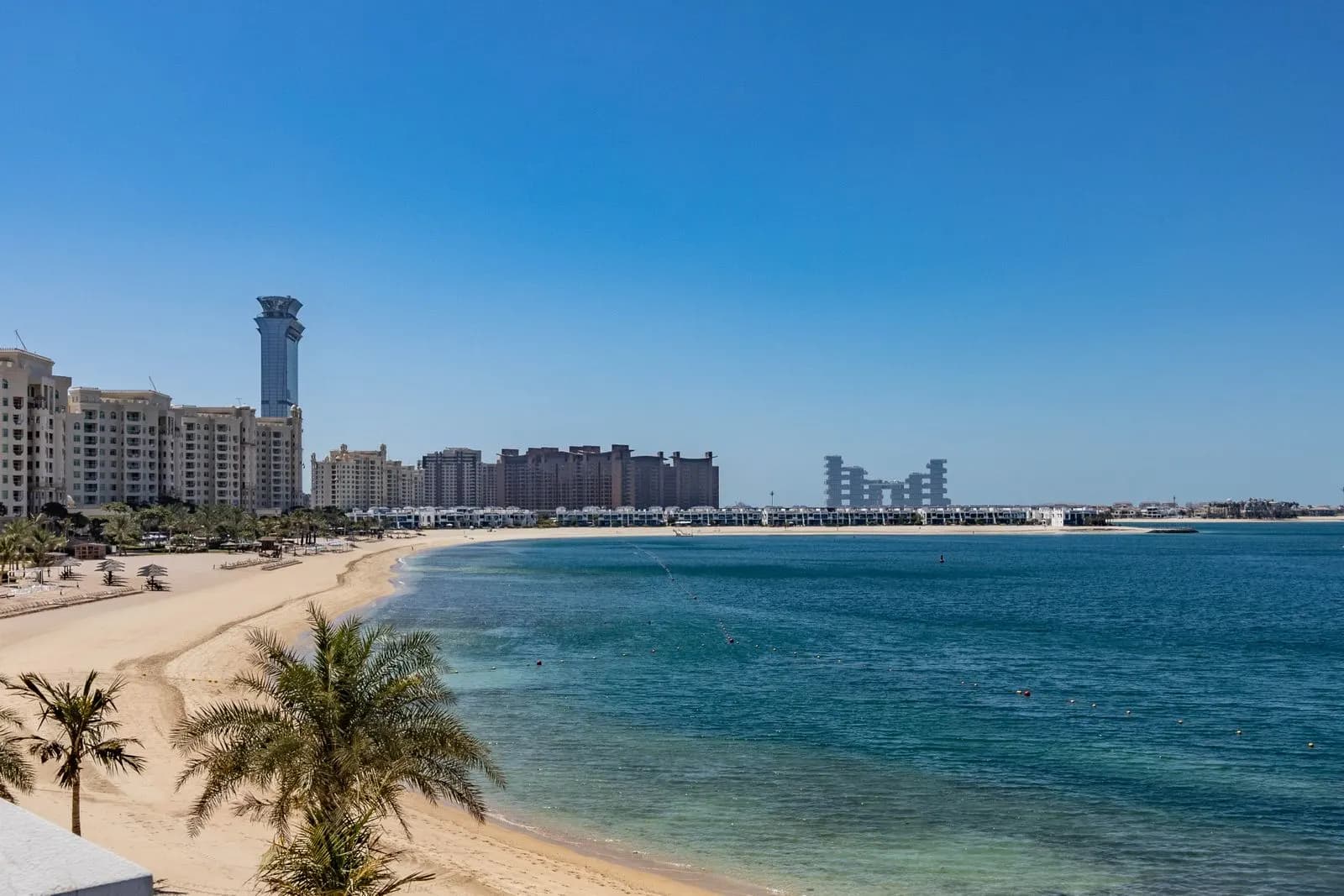 شاطئ في دبي بأشجار نخيل ومبانٍ منخفضة على امتداد الساحل.