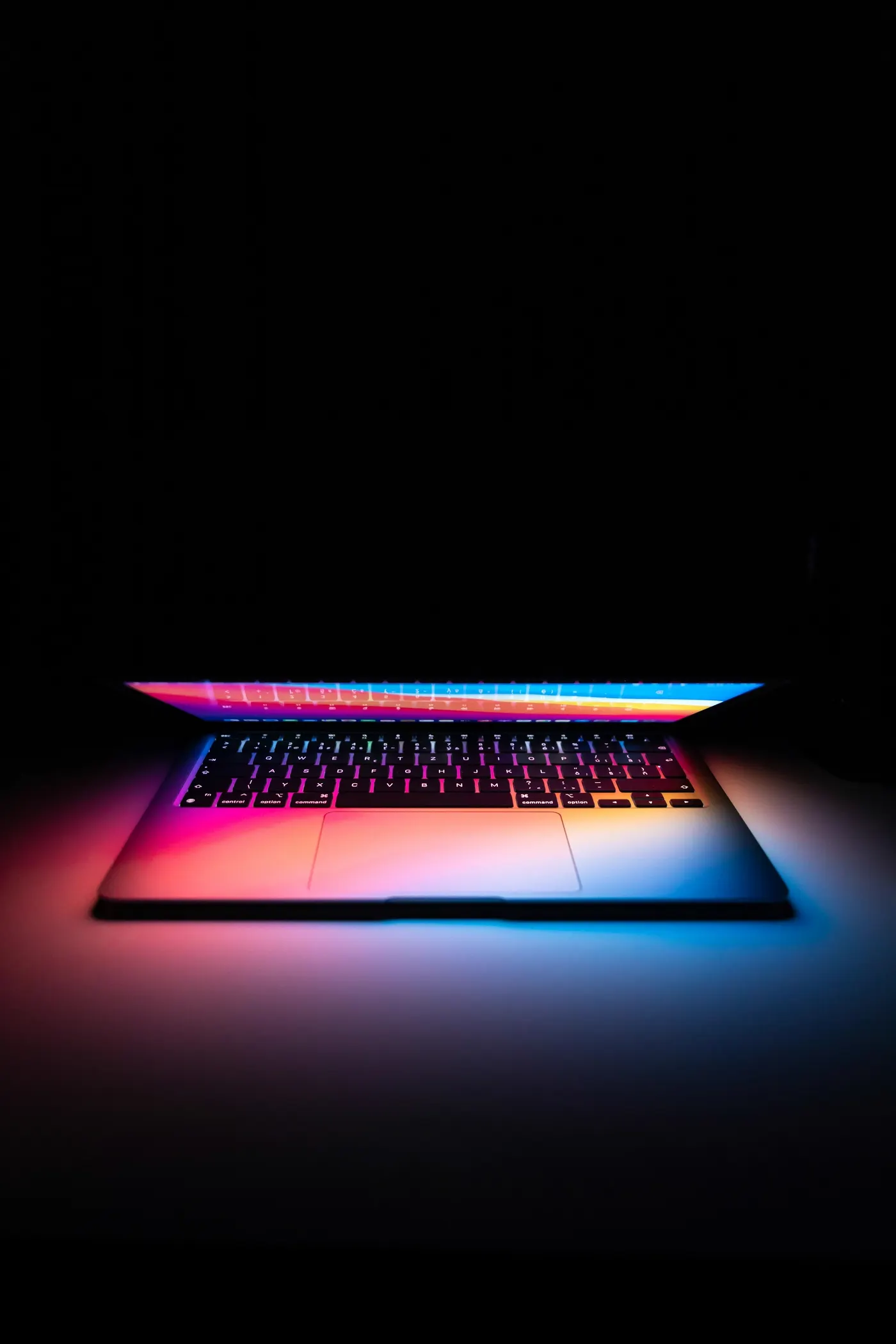 A laptop keyboard glowing with coloured light in a darkened room.