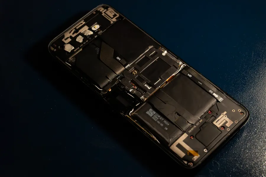 A disassembled smartphone on a dark surface with its battery and internal components exposed.