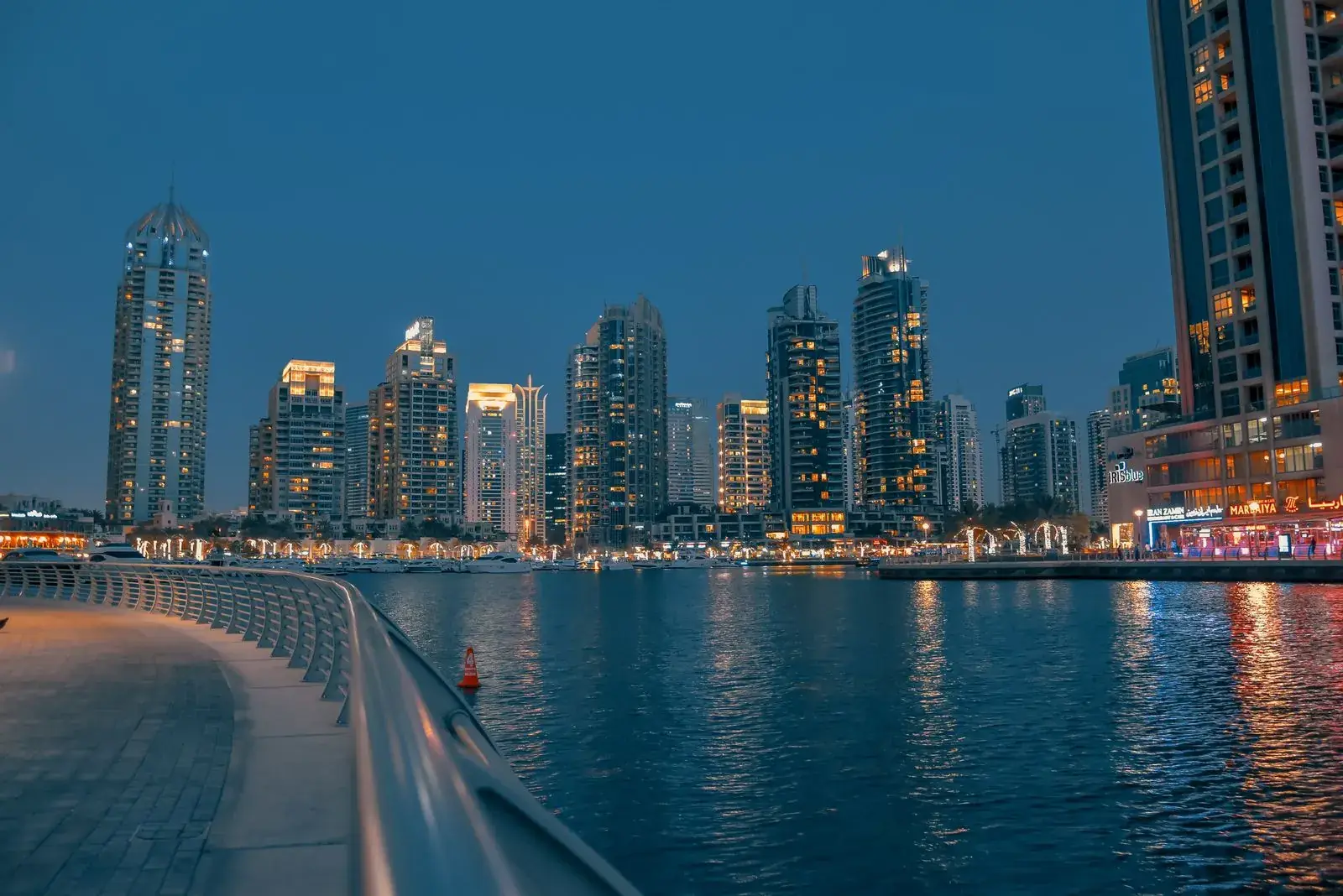 The Dubai Marina promenade at dusk, towers lit along the water.